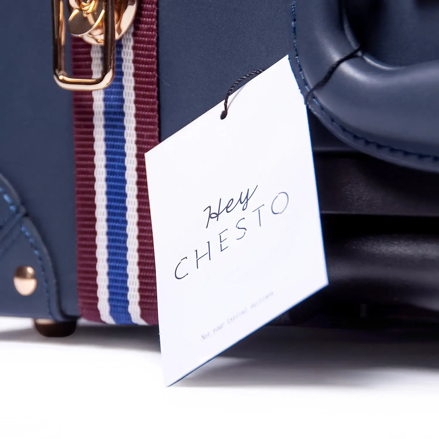 Navy vegan leather bag with striped strap and 'Hey CHESTO' tag, minimalist luxury design